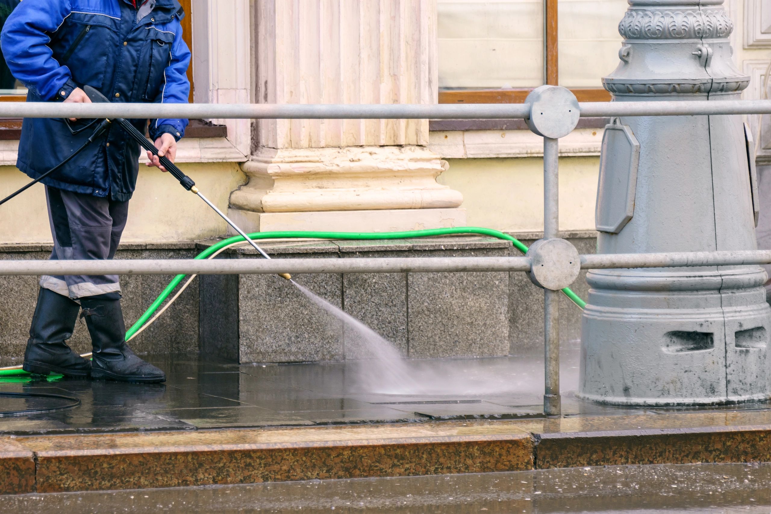 Worker pressure washing surface in front of building